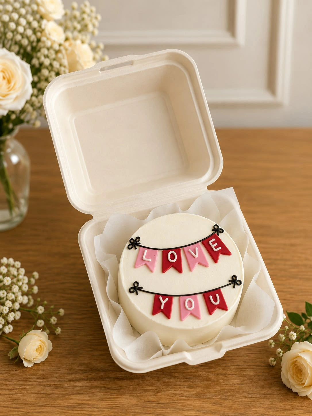 White single-tier bento cake in clamshell box featuring two tiers of festive love you bunting flags