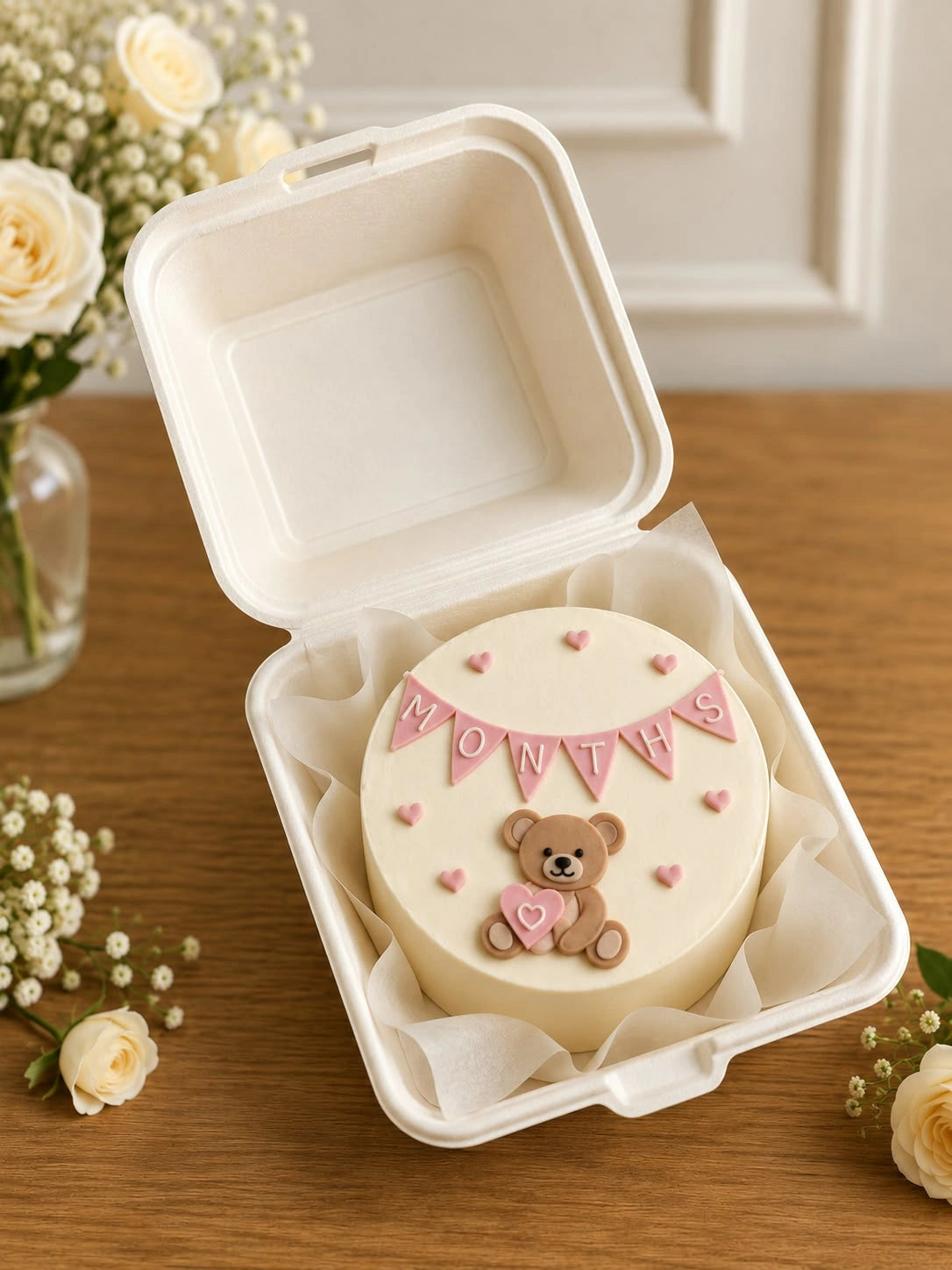 Cream bento cake with sculpted teddy bear holding heart and pastel pink months bunting garland
