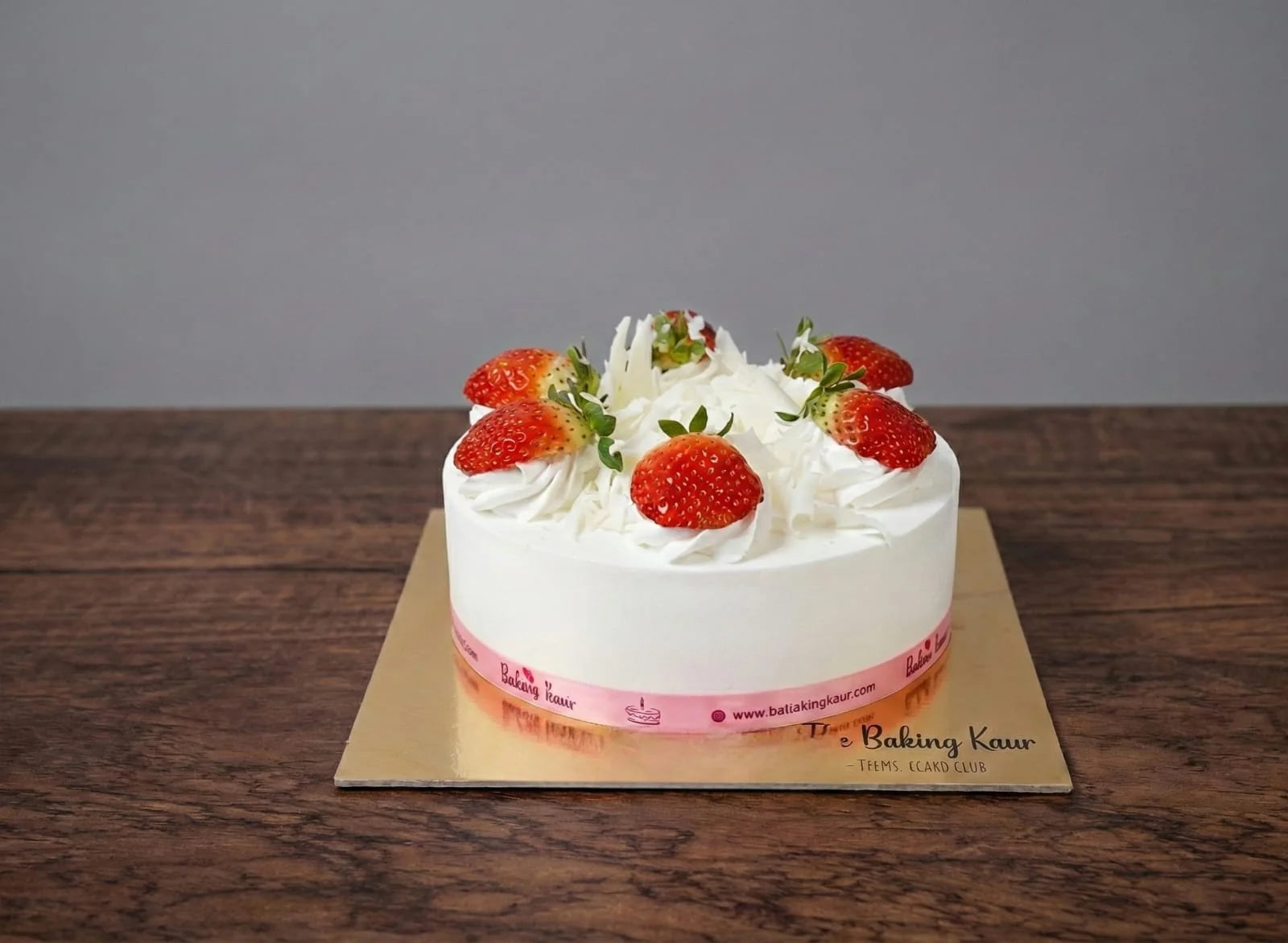 White cake with strawberries on a wooden board against a gray background